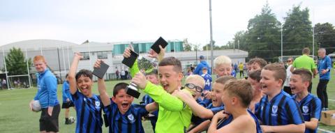 Oxford United Stars FC celebrating wining a football match. One young person is holding a small trophy and the others are crowded around him cheering
