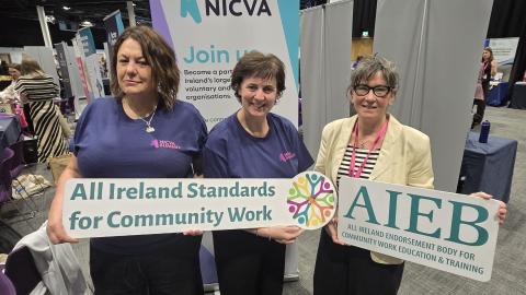 NICVA Staff with a representative of AIEB holding signs of the AIEB logo and a slogan, All Ireland Standards of Community Work