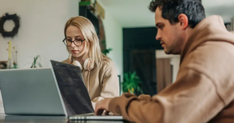 blonde woman and dark-haired man both working on laptops