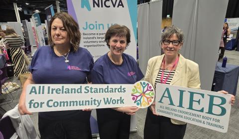 NICVA Staff with a representative of AIEB holding signs of the AIEB logo and a slogan, All Ireland Standards of Community Work